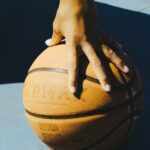 A hand resting on a basketball outdoors, capturing a moment of sport and leisure.
