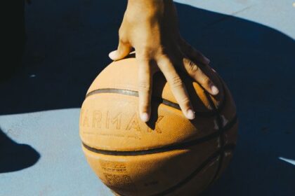 A hand resting on a basketball outdoors, capturing a moment of sport and leisure.