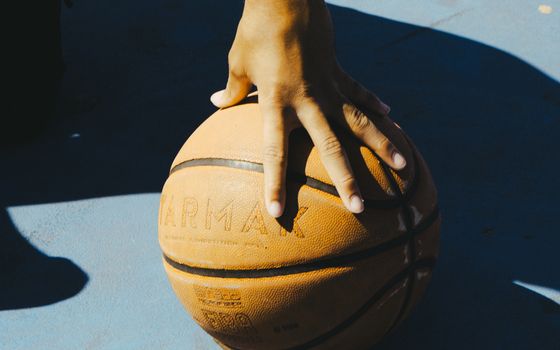 A hand resting on a basketball outdoors, capturing a moment of sport and leisure.