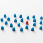 A red meeple stands out in a pattern of blue figures, symbolizing individuality.