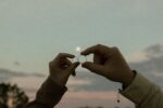 Two hands holding marriage rings at sunset, symbolizing love and commitment.