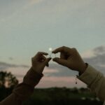 Two hands holding marriage rings at sunset, symbolizing love and commitment.