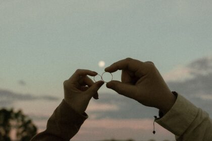 Two hands holding marriage rings at sunset, symbolizing love and commitment.