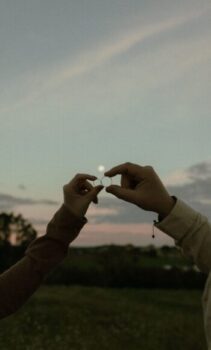 Two hands holding marriage rings at sunset, symbolizing love and commitment.