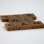Scrabble tiles spelling 'Yes We Can' on a white background, conveying encouragement.