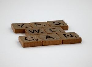 Scrabble tiles spelling 'Yes We Can' on a white background, conveying encouragement.